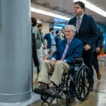 former Senate Republican Leader Mitch McConnell is assisted by an aide while using a wheelchair in the hallways of the U.S. Capitol complex. McConnell began regularly utilizing a wheelchair to navigate the Capitol following a series of health challenges and falls. Source: Getty Images North America / Congressional Pool Archive