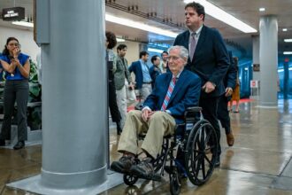 former Senate Republican Leader Mitch McConnell is assisted by an aide while using a wheelchair in the hallways of the U.S. Capitol complex. McConnell began regularly utilizing a wheelchair to navigate the Capitol following a series of health challenges and falls. Source: Getty Images North America / Congressional Pool Archive